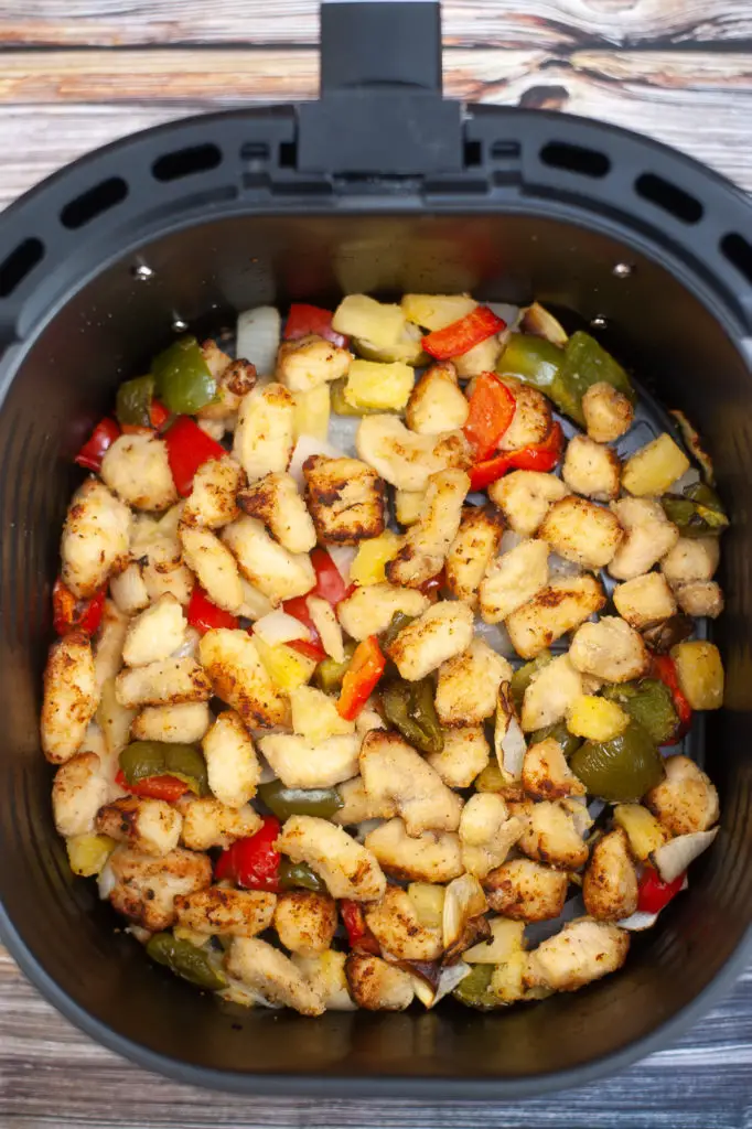 Cooked vegetables and cooked chicken in air fryer basket. 
