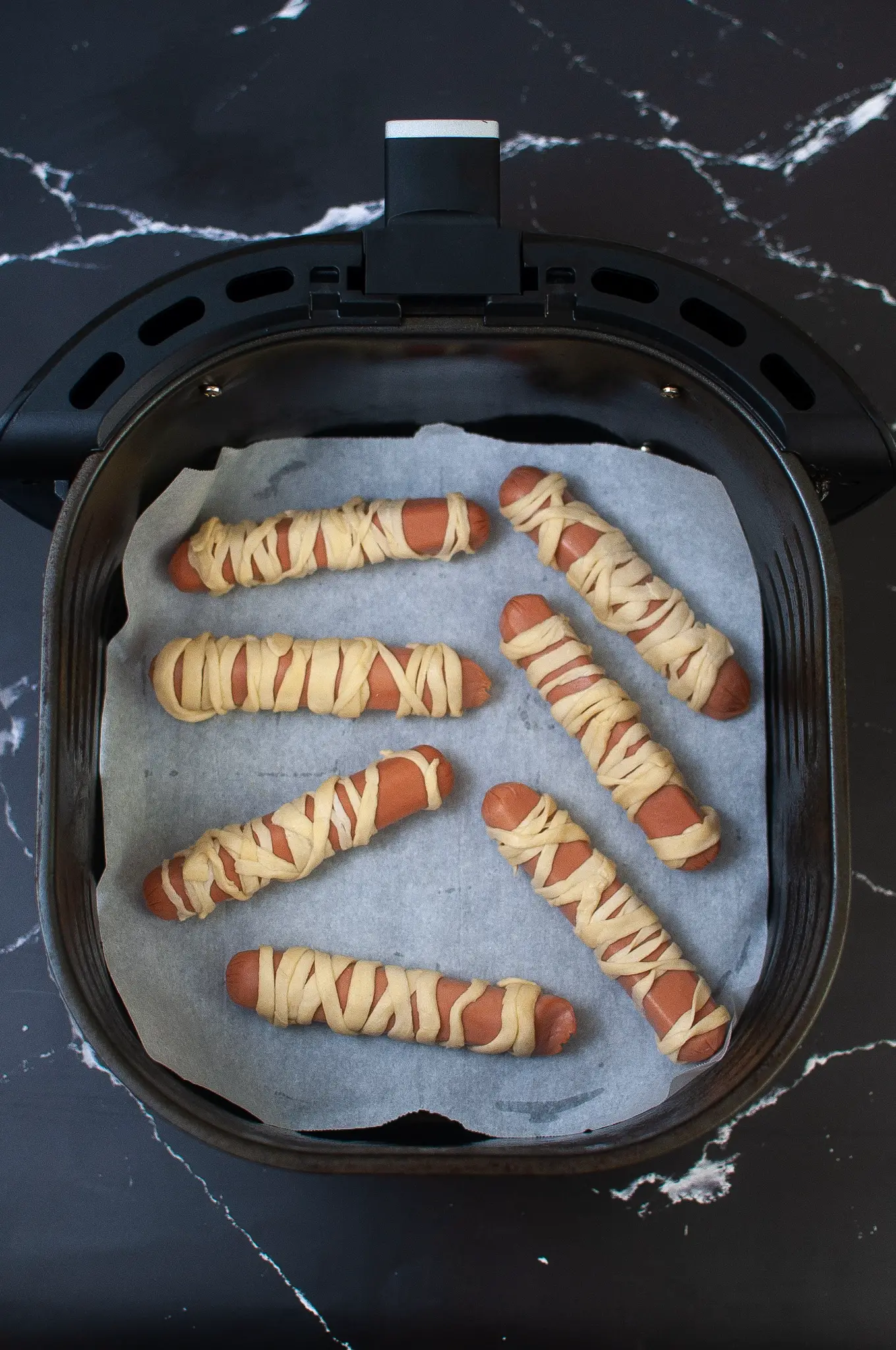 Hot dogs are wrapped in strips of crescent rolls strips, and placed in the Air Fryer