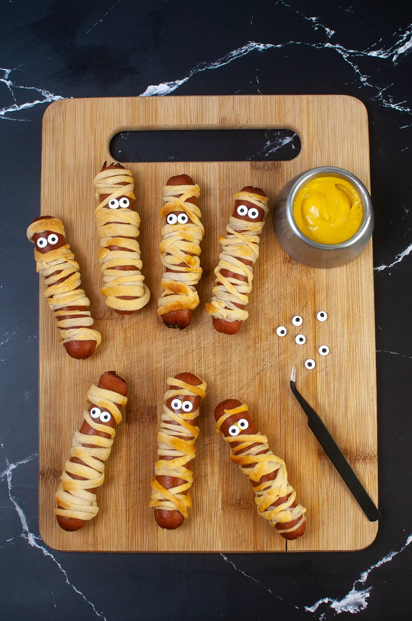 Mummy Dogs are on a cutting board with sugar eyeballs attached.