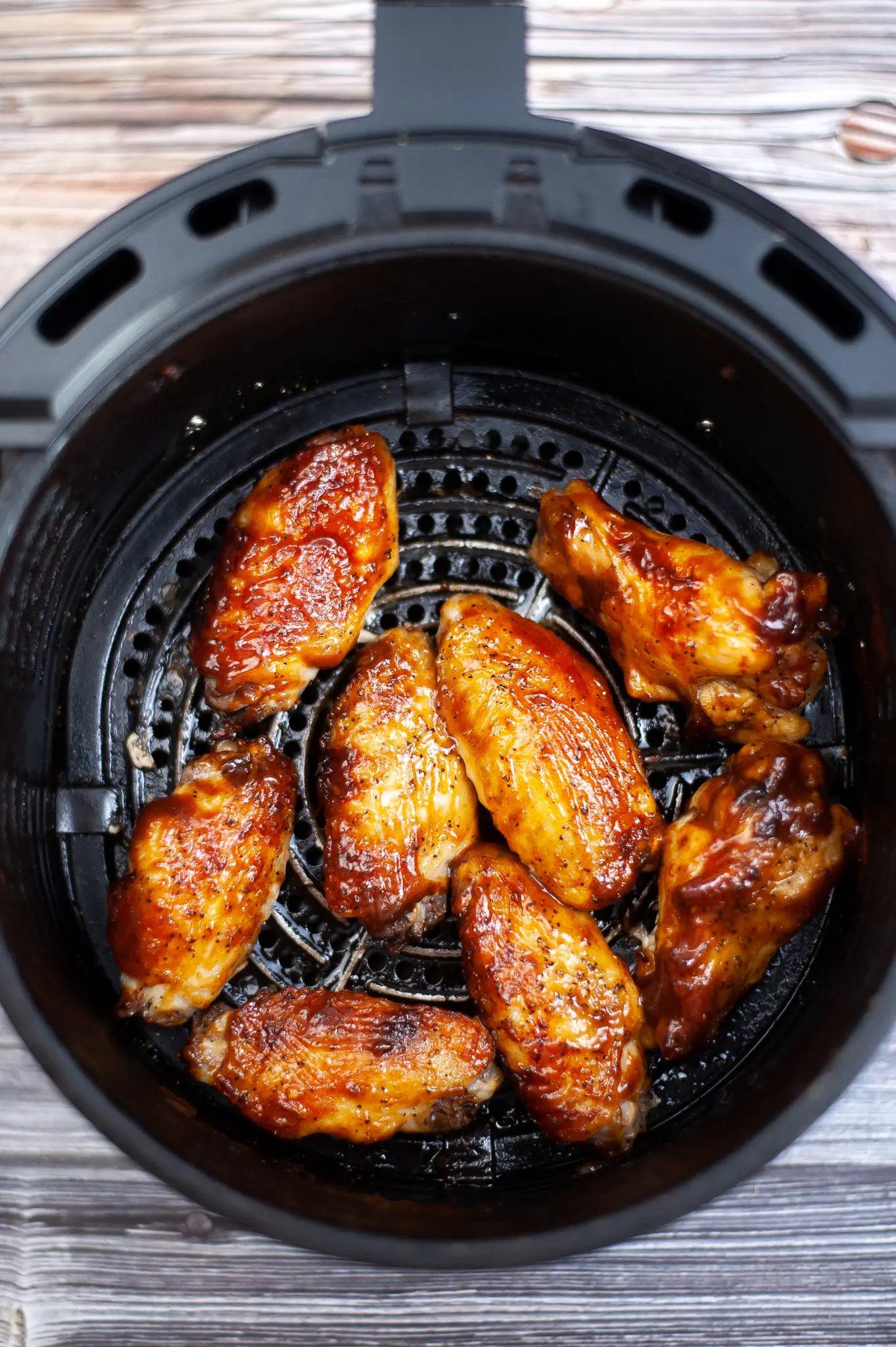 Chicken Wings in air fryer, cooked, coated in BBQ sauce.
